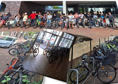 Das obere, panoramahafte Foto zeigt eine große, fröhliche Schülergruppe mit Fahrradhelmen und ihren Mountainbikes vor dem modernen Eingangsbereich der Schule, die gemeinsam in die Kamera winkt. Die unteren Aufnahmen zeigen verschiedene Perspektiven der dicht genutzten, überdachten und offenen Fahrradabstellanlagen auf dem Schulhof, was die umweltfreundliche und nachhaltige Mobilität der Jugendlichen im Schulalltag veranschaulicht.